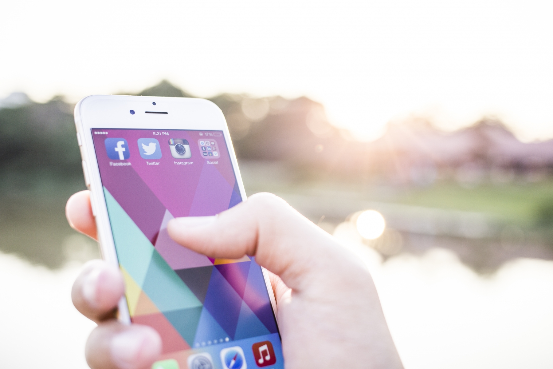 En hand håller en mobiltelefon där man ser ikonerna för Facebook, Twitter och Instagram.